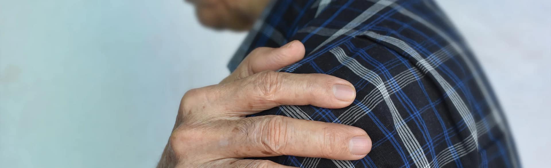 Older gentleman holding his shoulder due to suffering from Frozen Shoulder